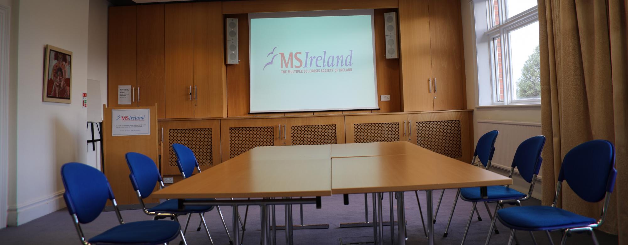 boardroom with a large screen, conference table, and chairs arranged around the desk