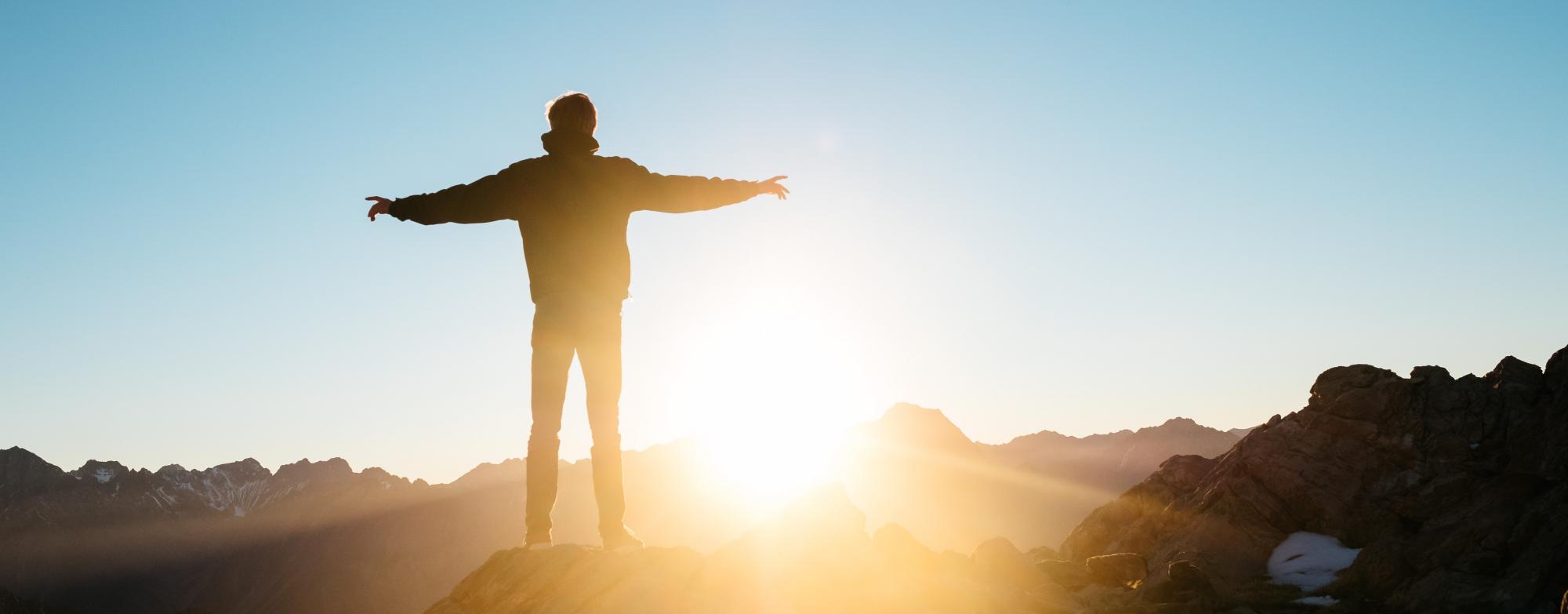 Image of a person standing with their arms open at a sunrise. 