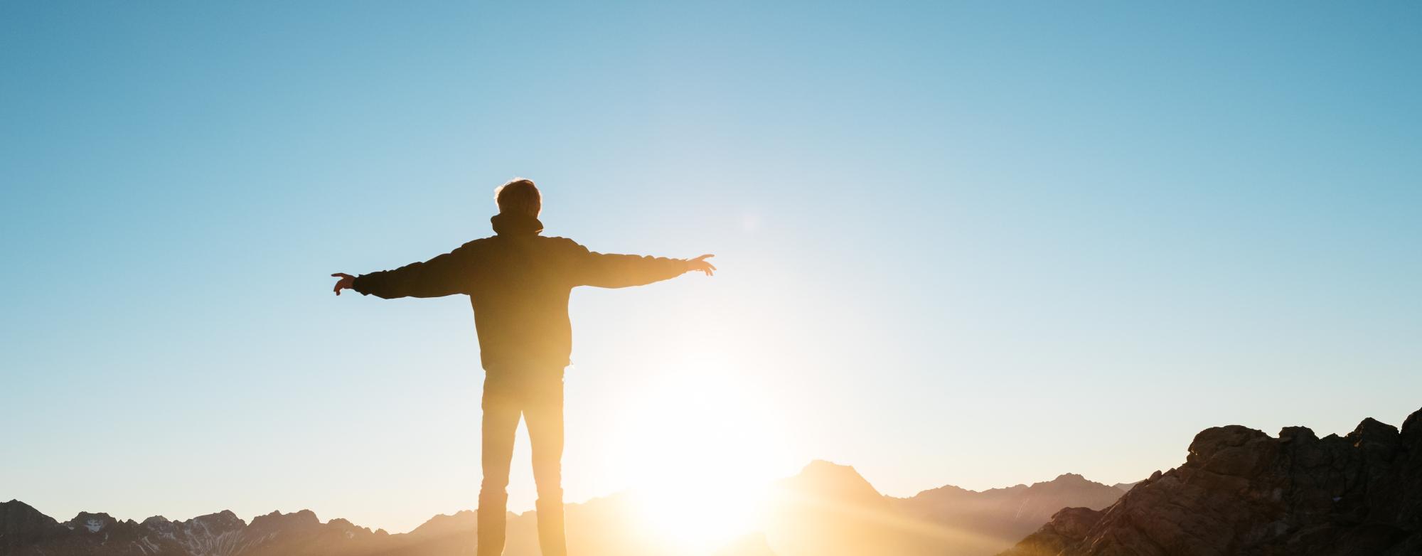 Image of a person standing with their arms open at a sunrise. 