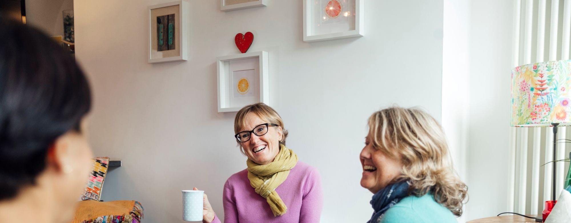 A small group of people sitting together, talking and sharing tea in a relaxed, supportive setting.