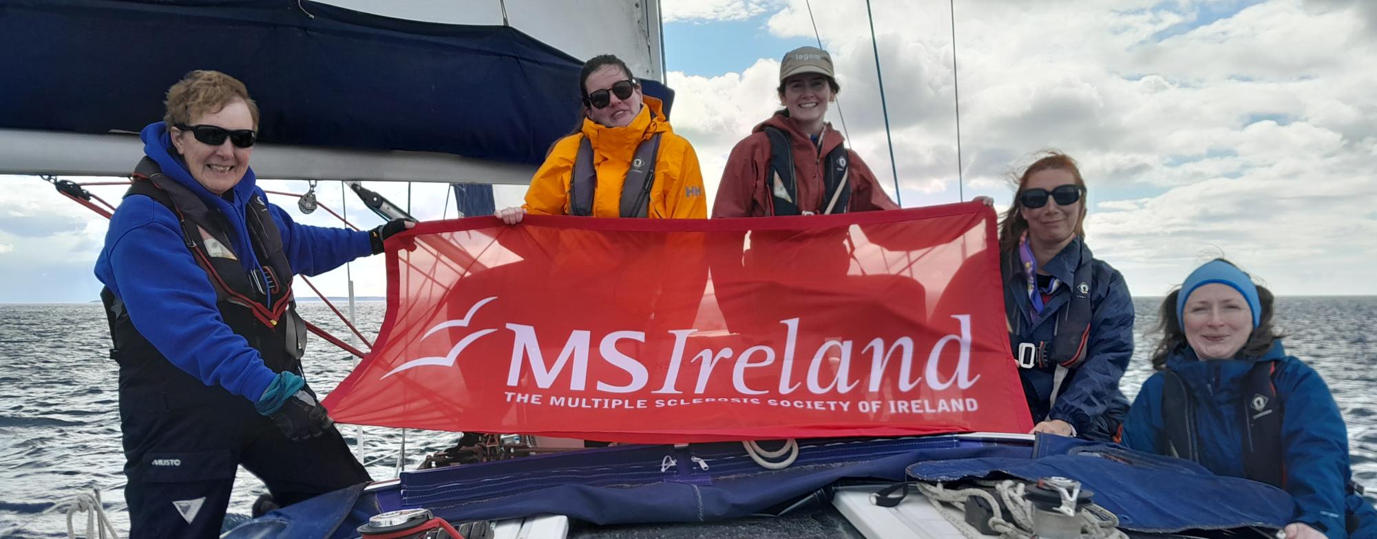 Participants on a sailing boat holding an MS Ireland banner during the 2026 Sailing Programme.