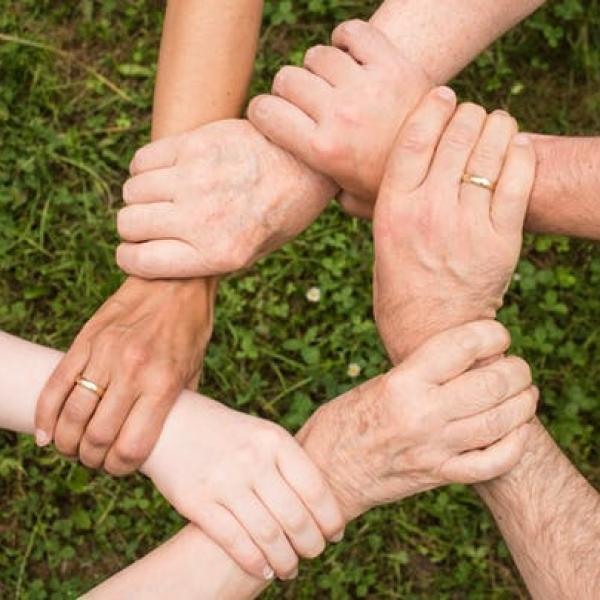 Image of 6 hands intertwined and holding each others wrists in a circle shape.