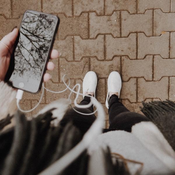 Person holding a smartphone and listening to a podcast through earphones.
