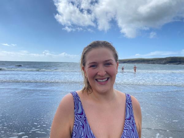 Person standing by the shore in swimwear, under a blue sky with white clouds.