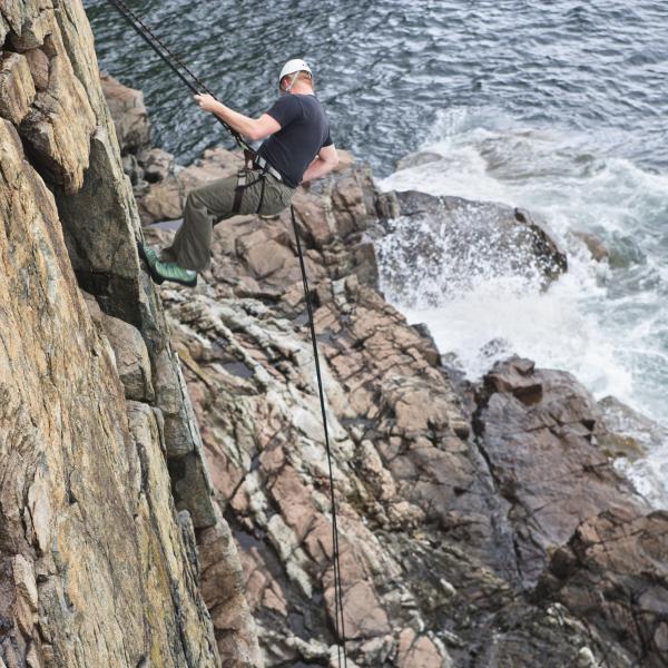 Person abseiling down the limestone cliffs of the Burren National Park with water visible below