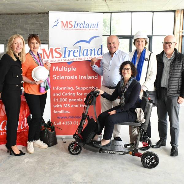 Group at MS Ireland Limerick launch, showcasing plans for new centre; one woman seated on a mobility scooter.