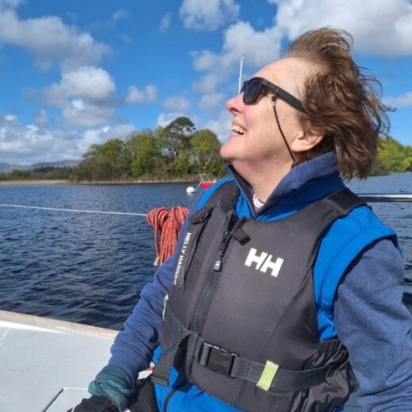 Shirley Foley smiling while sailing on a lake, wearing a life jacket on a sunny day.