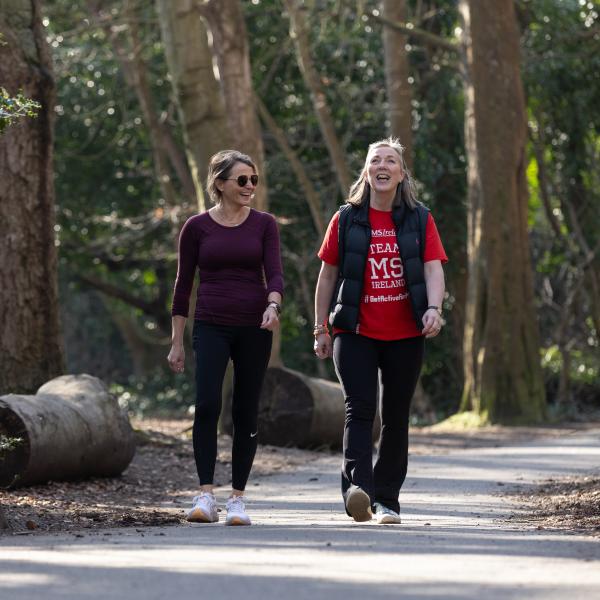 Two people walking and smiling together along a wooded park path during a STEPtember fundraising event.