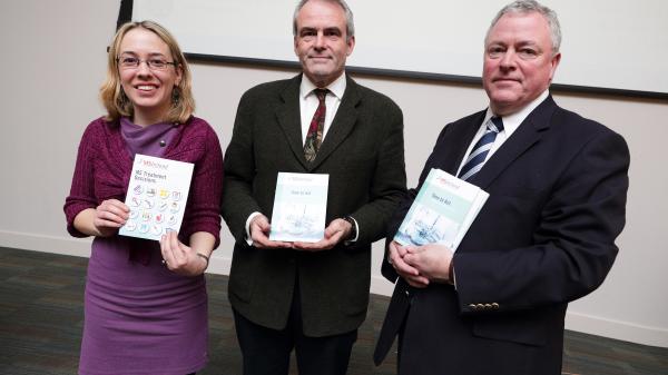 Three people standing together, each holding a copy of the new publication 'Time to Act,' smiling and posing for a photo