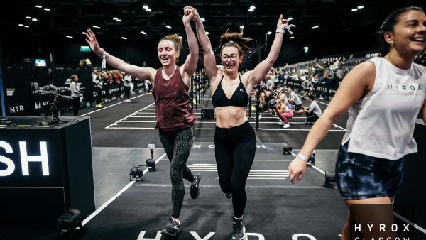 Two people holding hands raised in the air, celebrating as they cross the finish line of a Hyrox event