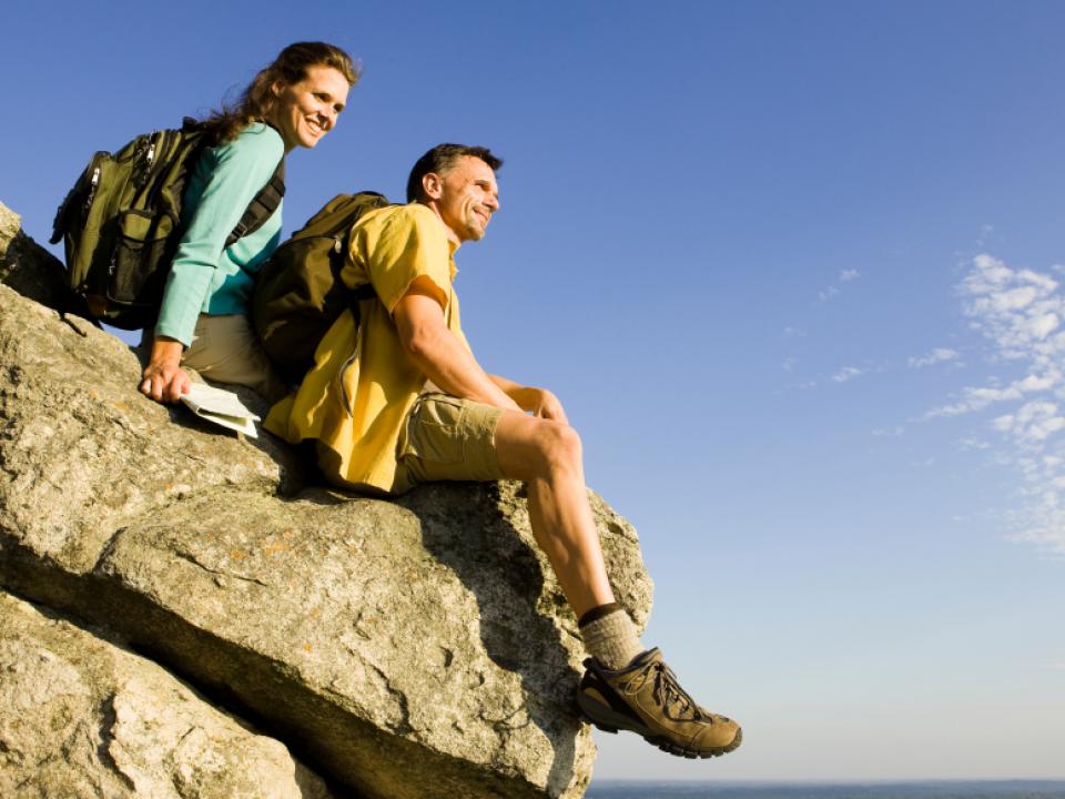 Image of two people with backpacks sitting on a rock with a blue sky background
