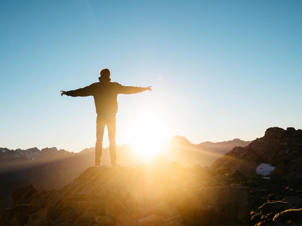 Image of a person standing with their arms open at a sunrise. 