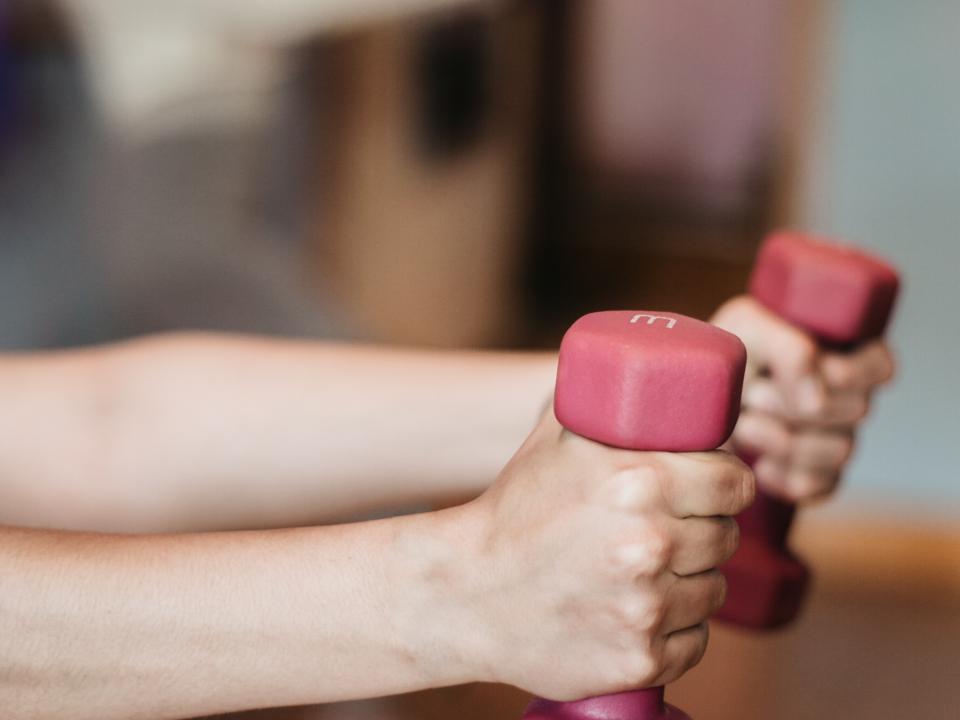 Person with arms outstretched, holding weights in each hand, performing an exercise or strength training