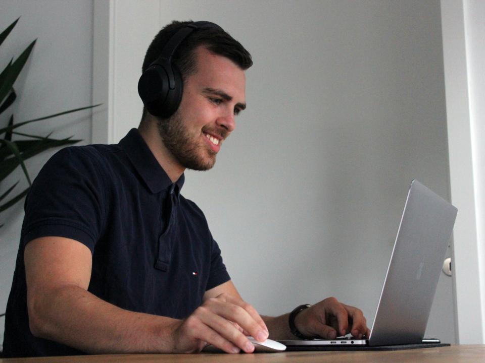 man wearing headphones and smiling while working on a laptop