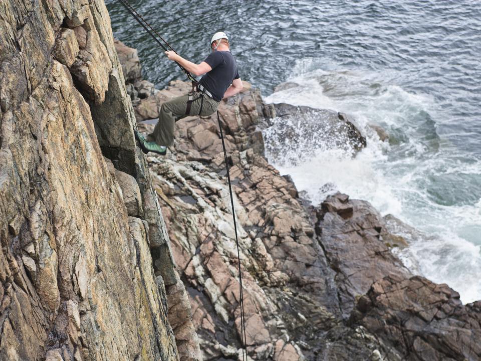 Person abseiling down the limestone cliffs of the Burren National Park with water visible below