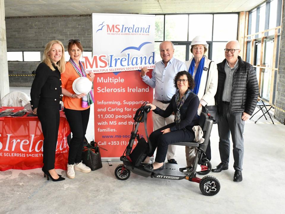 Group at MS Ireland Limerick launch, showcasing plans for new centre; one woman seated on a mobility scooter.