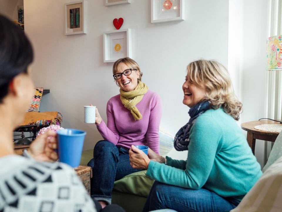 A small group of people sitting together, talking and sharing tea in a relaxed, supportive setting.