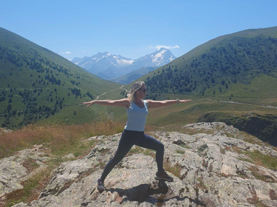 Samantha McCarthy outdoors on a mountain landscape, standing confidently with arms outstretched.