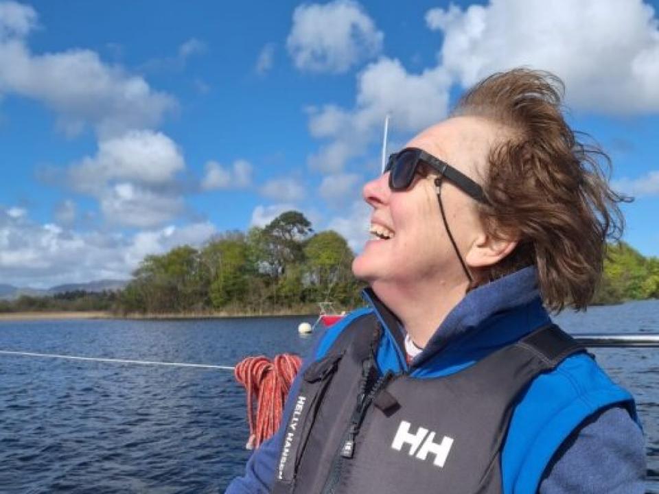 Shirley Foley smiling while sailing on a lake, wearing a life jacket on a sunny day.