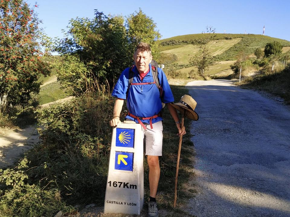 Hiker beside a Camino de Santiago marker reading "167 km" in the rolling hills of Castilla y León.