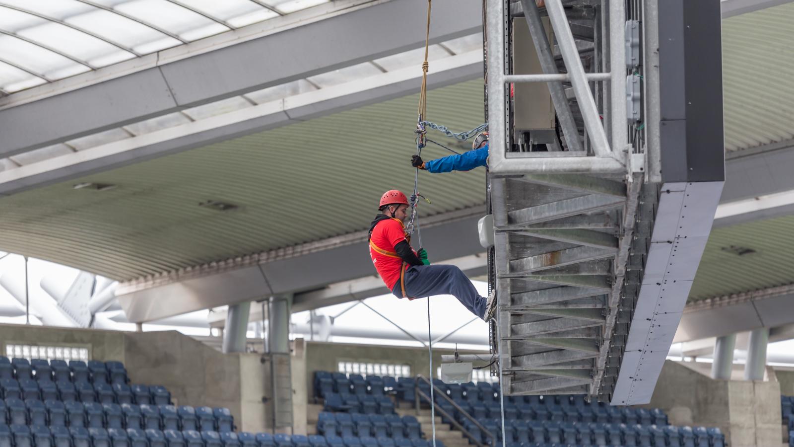 A person wearing a red t-shirt abseiling down from a great height at Croke Park, with a clear view of the stadium and ground far below