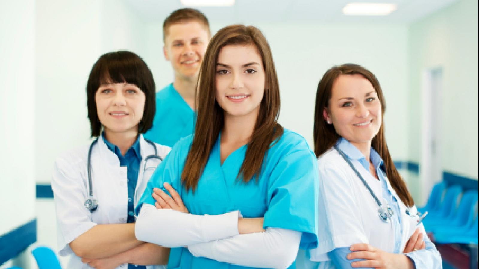 Four healthcare professionals in scrubs looking to camera with their arms crossed .