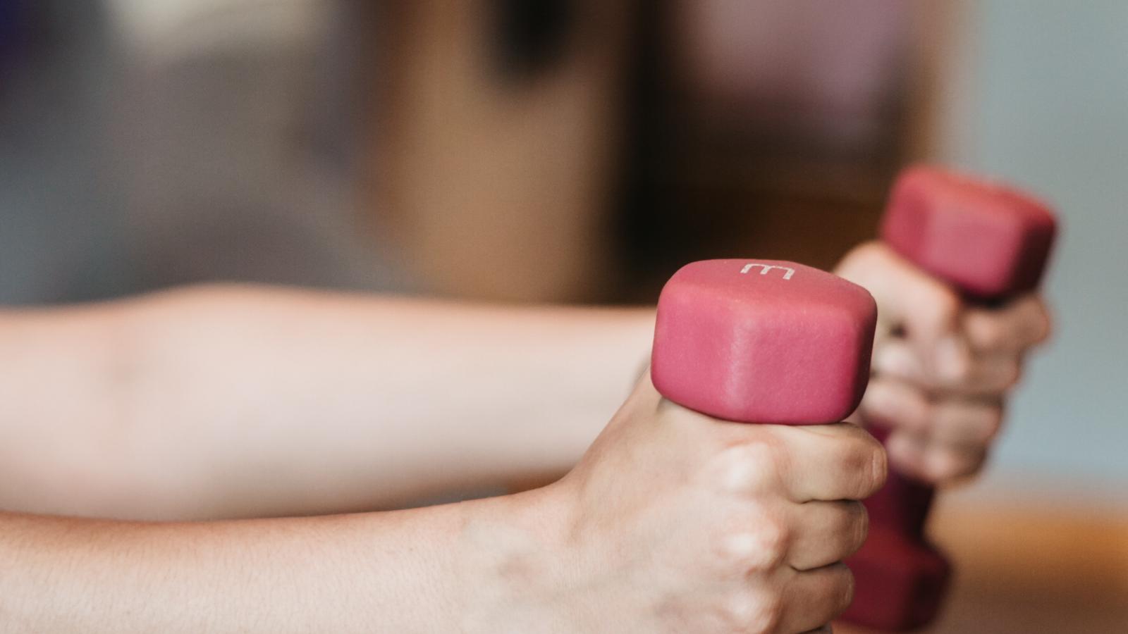 Person with arms outstretched, holding weights in each hand, performing an exercise or strength training