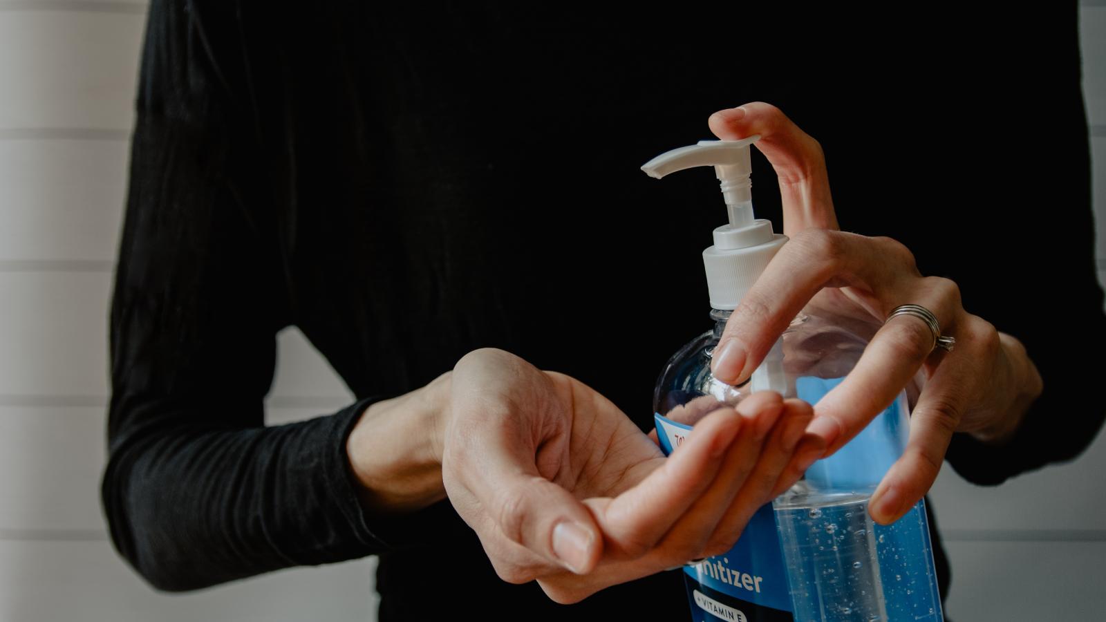 Someone in a black top and blue jeans standing holding a bottle of liquid soap, dispensing it with a pump lid. 