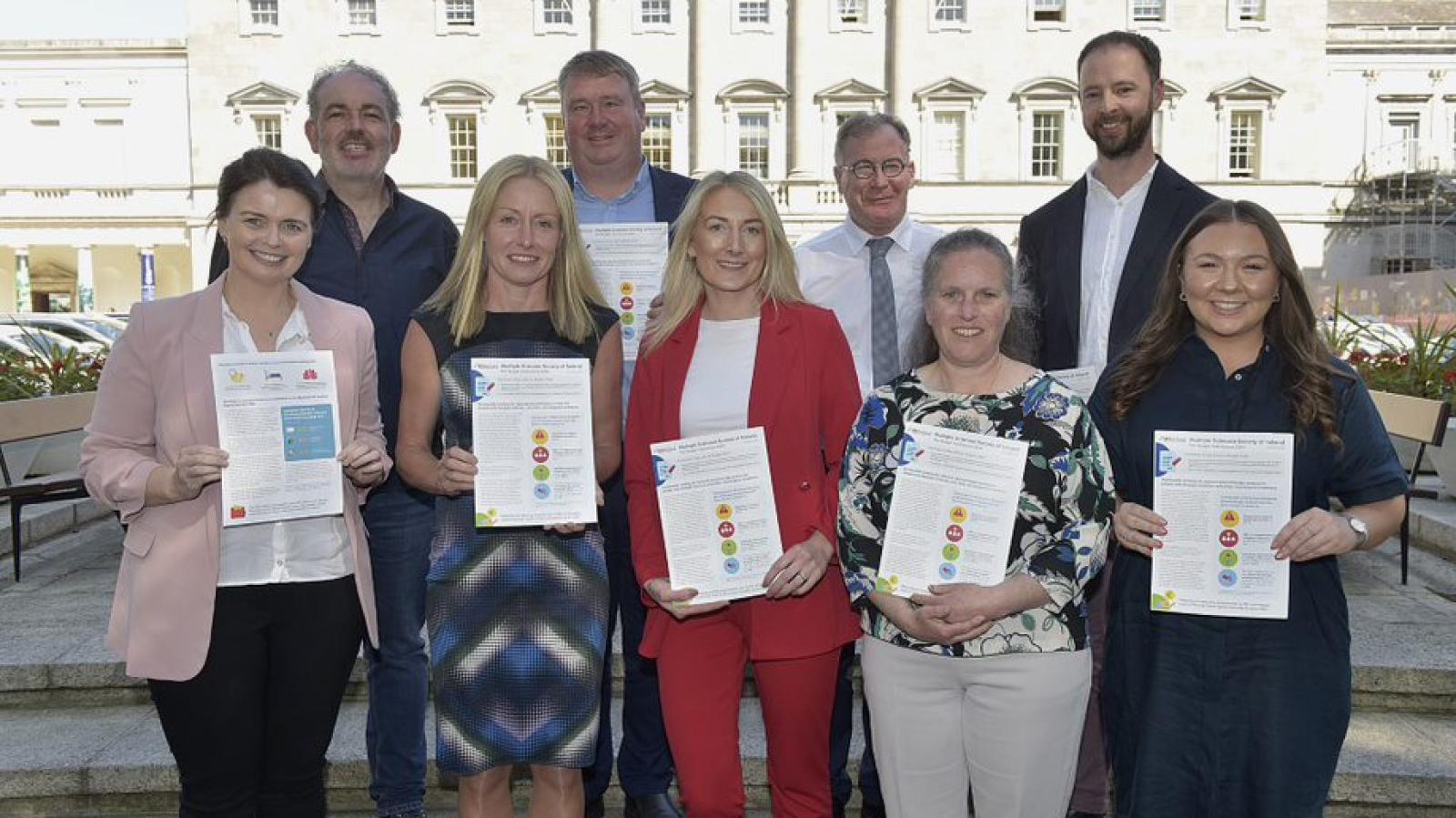Photo of a group of individuals outside Leinster House. They are holding documents to camera. 