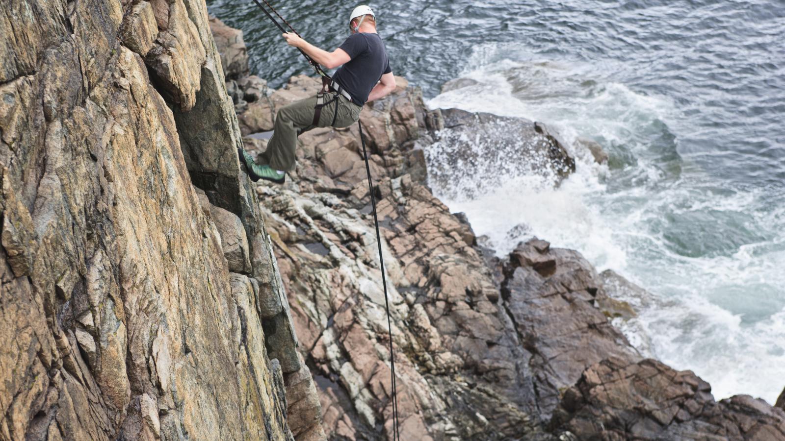 Person abseiling down the limestone cliffs of the Burren National Park with water visible below