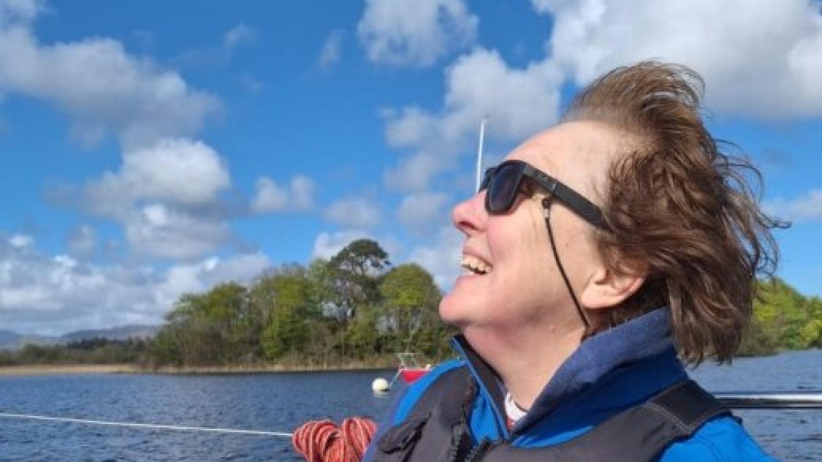 Shirley Foley smiling while sailing on a lake, wearing a life jacket on a sunny day.